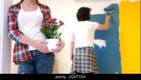 Glückliches Paar Haupterneuerungen zu tun, ist der Mann das Zimmer und die Frau halten den Topf mit Blumen Malerei. Stockfoto