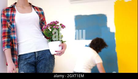 Glückliches Paar Haupterneuerungen zu tun, ist der Mann das Zimmer und die Frau halten den Topf mit Blumen Malerei. Stockfoto