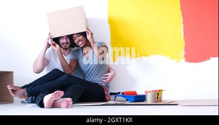 Glückliche junge multiethnischen paar entspannen und spielen mit Kartons nach einen Raum in ihrem neuen Haus auf dem Boden zu malen Stockfoto