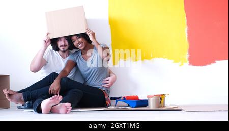 Glückliche junge multiethnischen paar entspannen und spielen mit Kartons nach einen Raum in ihrem neuen Haus auf dem Boden zu malen Stockfoto