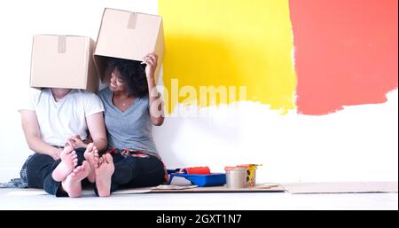 Glückliche junge multiethnischen paar entspannen und spielen mit Kartons nach einen Raum in ihrem neuen Haus auf dem Boden zu malen Stockfoto