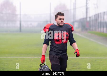 Junge zuversichtlich American Football Spieler mit einem schwarzen Helm bei einem Spaziergang durch das Stadion Feld nach einem harten Training Stockfoto