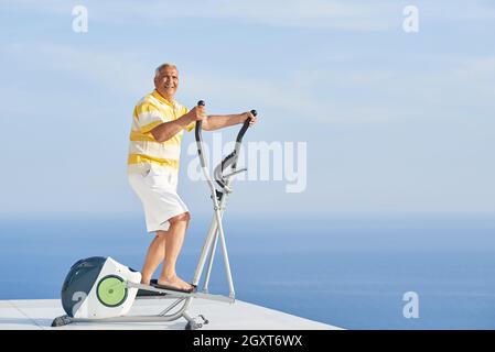 gesunde Senioren Mann arbeiten auf Fitness Laufband Maschine im modernen Haus Terrasse mit Meerblick Stockfoto