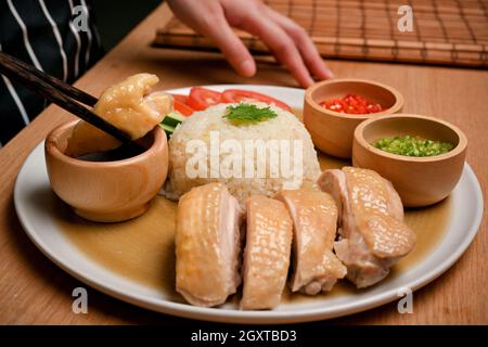 Nahaufnahme von weiblichen gebrauchten Essstäbchen, um sich ein wenig Hühnchen in süßer Sojabohnensauce zu holen. Hainanese-Hühnerreis Stockfoto