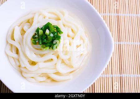Frisch zubereitete japanische udon-Nudeln in einer weißen Schüssel mit Frühlingszwiebeln garniert auf Bambusmatte. Stockfoto