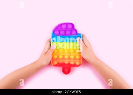 Kinderhände halten farbige Pop it Anti-Stress-Spielzeug isoliert auf rosa Hintergrund. Nahaufnahme. Stockfoto
