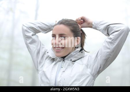 Glückliche Wandererin, die mit ihren Haaren einen Pferdeschwanz macht Ein nebliger Wald bereit zu gehen Stockfoto