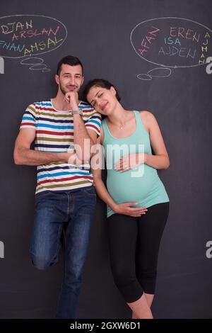 Junge schwangere paar Gedanken über Namen für Ihr ungeborenes Baby und sie schreiben auf eine Schwarze Schiefertafel Stockfoto