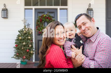 Glückliche junge Familie auf der Veranda des Hauses mit Weihnachtsschmuck. Stockfoto