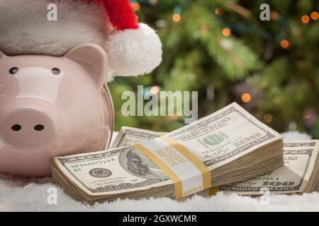 Piggy Bank tragen Santa Hat in der Nähe von Stapel Hundert-Euro-Scheine auf Schneeflocken. Stockfoto