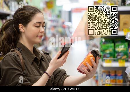 Junge schöne Frau scannt ein QR-Code-Produkt im Supermarkt. Das Konzept der modernen Technologie. Stockfoto
