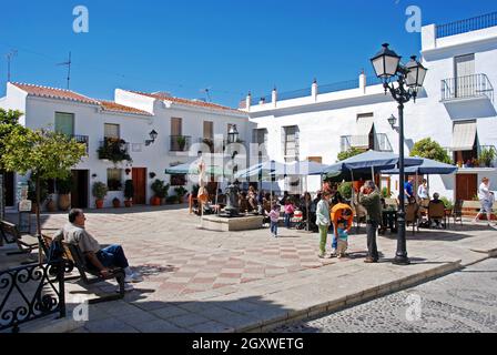 Menschen entspannen sich in Straßencafés auf dem Kirchplatz (Plaza de la Iglesia), Frigiliana, Spanien. Stockfoto