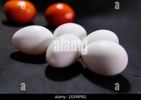 Fünf frische weiße Eier und Tomaten auf schwarzer Oberfläche Stockfoto
