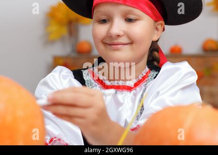 Halloween zu Hause feiern. Nahaufnahme eines kleinen Mädchens, das als Pirat gekleidet ist. Das Kind bereitet sich auf die Party vor und zieht den Kürbis an. Stockfoto