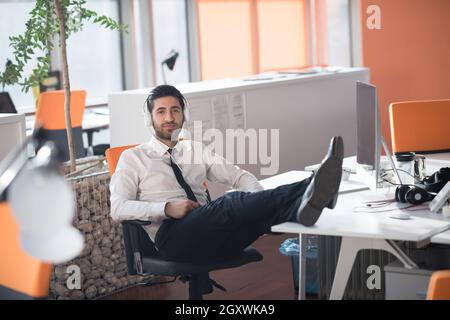 glückliche junge arabische Geschäftsmann mit Bart Musik hören über Kopfhörer in modernen Startup-Büro Stockfoto