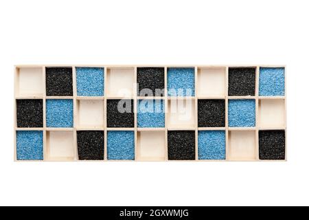 Holzkiste mit quadratischen Fächer teilweise mit blauen oder schwarzen Dekolack Sand gefüllt und einige leere Fächer. Stockfoto