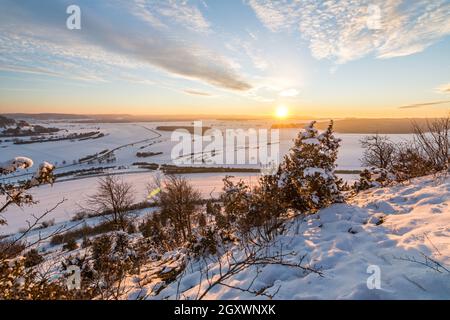 Szenischer Sonnenuntergang über verschneiten Winterlandschaften in den Schwäbischen Alpen mit Büschen und Bäumen im Vordergrund Stockfoto