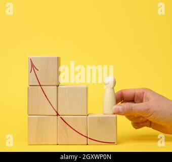 Die weibliche Hand hält eine Holzfigur auf einer Leiter aus Würfeln auf einem Gelee-Hintergrund. Konzept zur beruflichen Weiterentwicklung, Beförderung, persönliche Entwicklung, Coaching-Hilfe Stockfoto