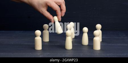 Weibliche Hand hält eine Holzfigur über der Menge. Das Konzept, Mitarbeiter, talentierte und einzigartige Mitarbeiter zu finden. Karriereentwicklung, Wahl des Ausstiegs Stockfoto