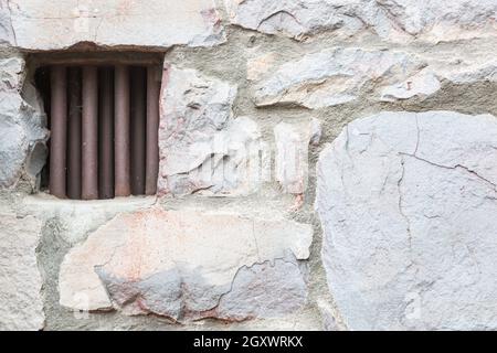 Alte Steinmauer mit kleinen eisernen Gefängniszelle Fenster gesperrt. Stockfoto