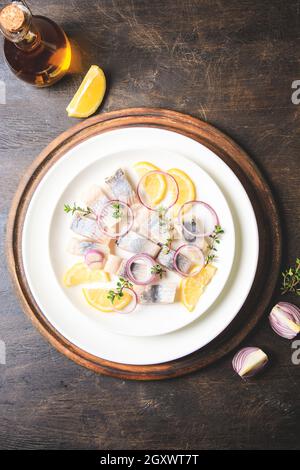 Gesalzener Hering mit Gewürzen, Kräutern und Zwiebel auf Teller auf Holzboden mit Kopierfläche. Marinierter Fisch in Scheiben. Essen mit gesunden ungesättigten Fetten, O Stockfoto