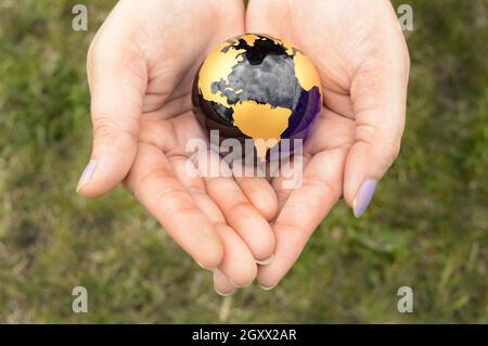 Der Erdglobus wird sicher in der Handfläche einer Frau gehalten, die die Hände über einem Grasbereich hält. Stockfoto
