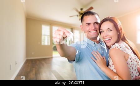 Junge militärische Paar mit Hausschlüssel im leeren Raum der neuen Heimat. Stockfoto