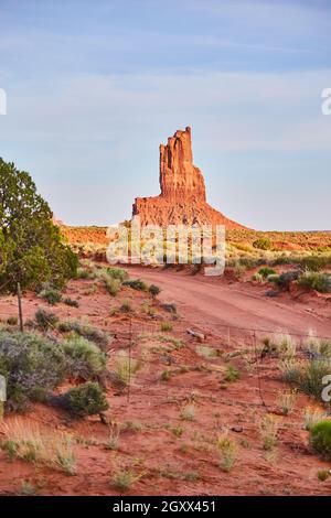 Dirt Road und Zaun in der Wüste neben der großen roten Felssäule Stockfoto