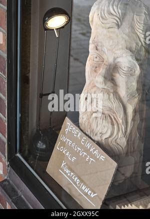 24. September 2021, Brandenburg, Frankfurt (oder): Im Fenster des Kunstshopfes 'Kukuryku' befindet sich eine Holzschnitzerei und ein Schild mit der Aufschrift 'jeder Einkauf unterstützt lokale Künstler'. Der Kunstladen befindet sich in einem ehemaligen DDR-Plattengebäude. In der deutsch-polnischen Partnerstadt Frankfurt (oder) - Slubice hat sich offenbar eine vielfältige Kunst- und Kulturszene entwickelt, die nur Insider kennen. Das wird sich mit dem Kunstladen 'Kukuryku ändern! Foto: Patrick Pleul/dpa-Zentralbild/dpa Stockfoto