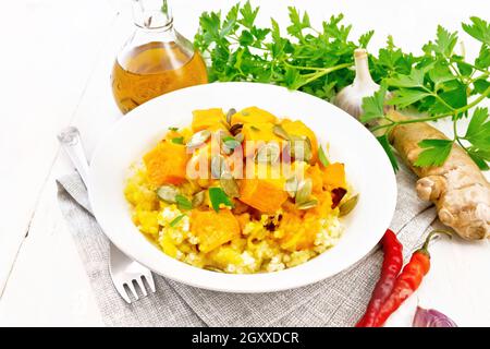 Hirsebrei mit würziger Kürbissauce und Samen auf einem Teller auf einem Küchentuch, Paprika, Ingwerwurzel, Knoblauch und Petersilie auf Holzbrett Backgrou Stockfoto