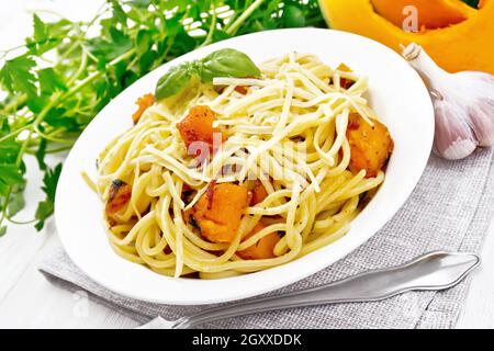 Spaghetti mit Kürbis, Zwiebel und Knoblauch auf einem Teller auf Serviette, Basilikum, Petersilie und Gabel auf weißem Holzbrett Hintergrund Stockfoto