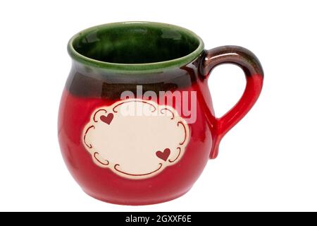 Nahaufnahme eines rot-grünen Keramikbechers mit einem leeren weißen Etikett und zwei kleinen Herzen darauf isoliert auf weißem Hintergrund. Valentine-Konzept. Makro. Stockfoto