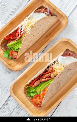 Tacos mit Schinken und Gemüse auf dem servierten Holzteller Stockfoto