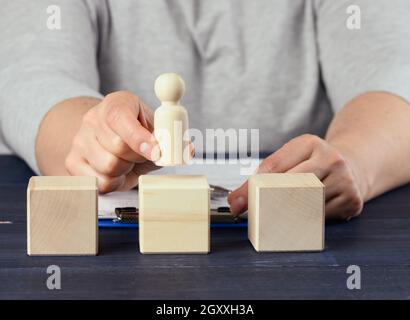 Weibliche Hand hält eine Holzfigur eines Mannes und legt einen Würfel auf. Promotion-Konzept, Coaching und Mentoring Stockfoto