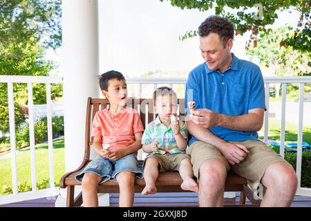 Kaukasische Vater sitzt mit seinem gemischten Rennen Chinesisch und kaukasischen Jungen genießen Eis Kegel Stockfoto