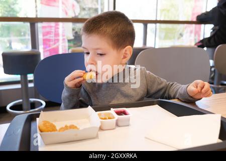 Ein Junge von 4 Jahren isst Nuggets mit Sauce in einem Fast-Food-Café. Stockfoto