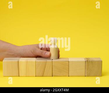 Weibliche Hand hält eine Holzfigur eines Mannes und legt einen Würfel auf. Promotion-Konzept, Coaching und Mentoring Stockfoto