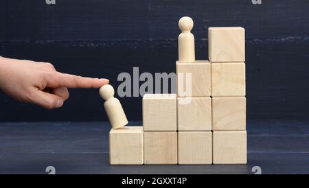 Weibliche Hand hält eine Holzfigur eines Mannes auf der ersten Stufe der Pyramide. Persönliches Wachstum, Unternehmensleiter, CEO, Mentoring Stockfoto