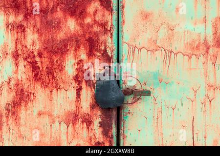 Nahaufnahme des Vorhängeschlosses und der alten Metallspange und der Klammer An einer rostigen Metalltür Stockfoto