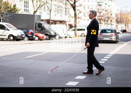 Blinden Mann zu Fuß auf dem Bürgersteig Holding Stick mit Armband Stockfoto