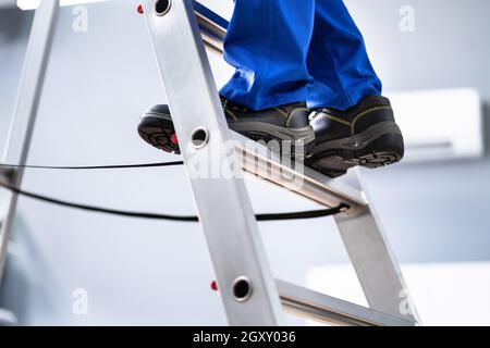 Mann In Schuhen Klettert Die Trittleiter. Sicherheit Und Versicherung Stockfoto