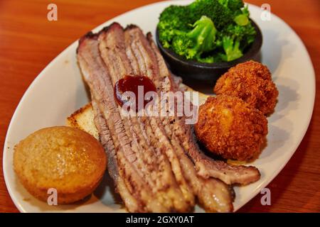 Brisket Scheiben mit einer Seite von Mais Muffin Hush Welpen und Brokkoli auf einem weißen Teller Stockfoto