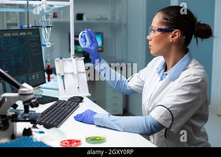 Biologin Forscherin Frau hält transparente Petrischale Analyse blaue Lösung während Biochemie Experiment. Wissenschaftler Arzt arbeitet mit dna-Probe im mikrobiologischen Krankenhauslabor Stockfoto
