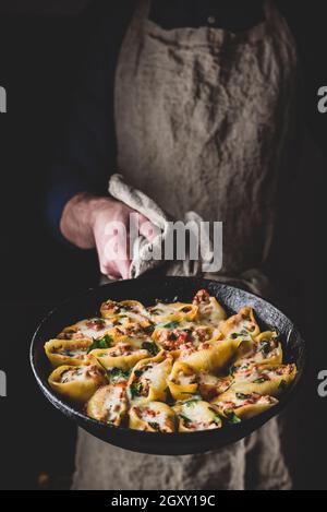 Der Küchenchef hält eine Pfanne mit gebackenen Jumbo-Shells-Pasta, gefüllt mit Hackfleisch, Spinat und Käse Stockfoto