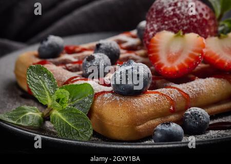 Köstliche Waffeln mit Puderzucker und Beeren auf schwarzem Keramikplatte auf grauem Hintergrund. Süße Mahlzeit. Nachtisch. Serviert werden Speisen Stockfoto