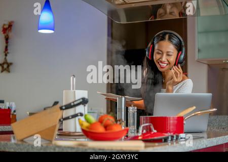 Beschäftigt glückliche Frau Betreiber Berater Service Arbeit durch Gespräche in Videokonferenz online mit einem Kopfhörer und Mikrofon. Ein Laptop in der Küche während c Stockfoto