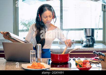 Beschäftigt glückliche Frau Betreiber Berater Service Arbeit durch Gespräche in Videokonferenz online mit einem Kopfhörer und Mikrofon. Ein Laptop in der Küche während c Stockfoto
