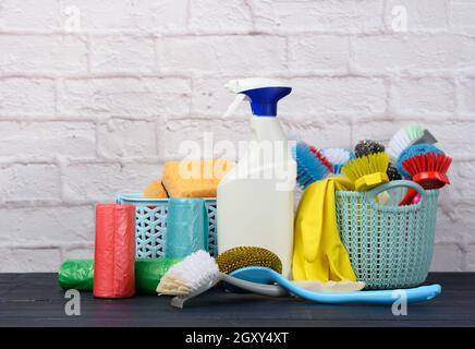 Schwämme, Plastikbürsten und Waschmittelflaschen auf einem blauen Holztisch. Haushaltsreinigungsgegenstände auf weißem Backsteinwand Hintergrund Stockfoto