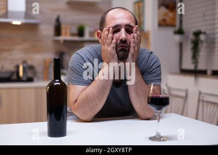 Verzweifelter Mann, der sich unglücklich fühlte, als er allein Glas mit Wein und Flasche trank. Person mit ungesunder sucht sitzt mit Alkohol, Alkohol, alkoholisches Getränk verärgert Stockfoto