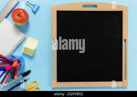 Flat Lay mit Schulkonzept auf blauem Hintergrund mit verschiedenen Schulzubehör, Stiften, Bleistift, Notizblock, Büroklammern, apfel, Lineal, Schere, leer Stockfoto